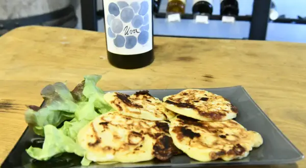 Assiette de migliacci dorés, accompagnés de salade verte, avec une bouteille de vin en arrière-plan. Une recette simple et savoureuse.