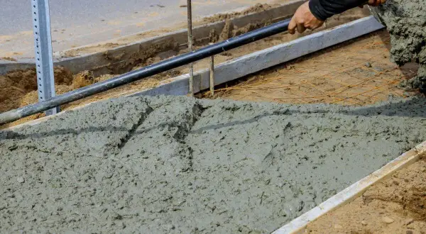 Prace budowlane: świeży beton, który będzie miał fakturę betonu szczotkowanego, jest rozkładany łopatą.