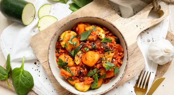 Gnocchi mit Spinat und Zucchini in Tomatensauce, garniert mit schwarzen Sesam.