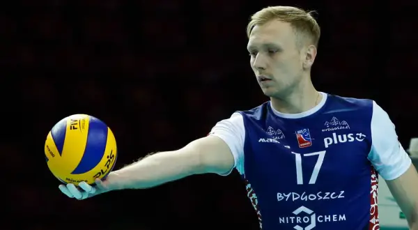 Siatkarz Mateusz Sacharewicz z piłką w dłoni, gotowy do zagrywki.