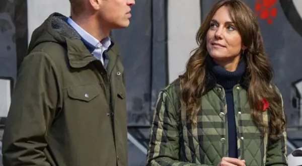 William van Wales y Kate Middleton, ambos con chaquetas, conversan frente a un mural.