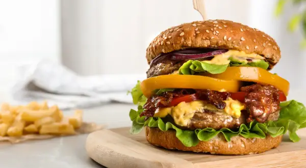 Soczysty burger z wołowiny z dodatkami na desce, obok frytki.