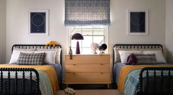 Twin beds with colorful quilts and star charts create fun boys bedroom ideas. A wooden dresser holds globes and a lamp.