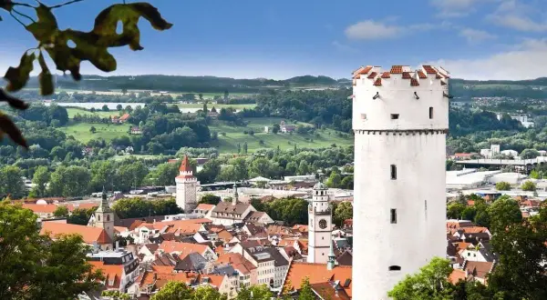 Der weiße Mehlsack Ravensburg ragt über die roten Dächer der Stadt. Im Hintergrund grüne Hügel und blauer Himmel.