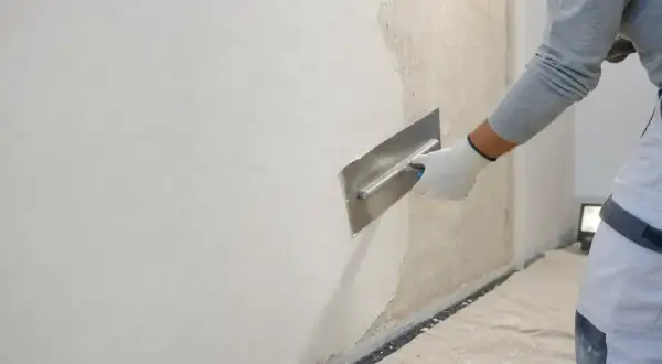 Lavoratore con spatola effettua rasatura muro esterno con rete, creando una finitura liscia e uniforme.