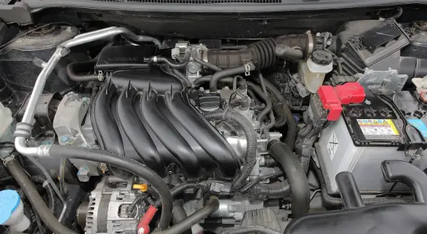 Silnik Nissan Qashqai J10, z widocznym kolektorem dolotowym, akumulatorem i alternatorem.