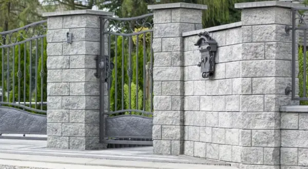 Betonowy słupek z zamontowaną skrzynką na listy i fragmentem metalowej furtki.
