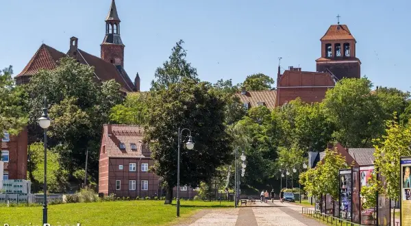 Tczew atrakcje: zabytkowy kościół, urokliwe kamieniczki i zielony park. Spacerowicze cieszą się słonecznym dniem.