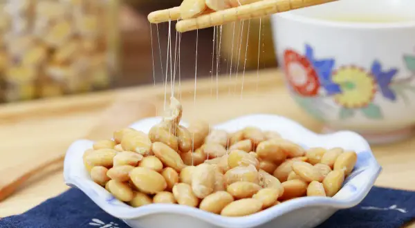 Fermentierte Sojabohnen, auch Natto genannt, werden mit Stäbchen aus einer Schale gehoben. Die klebrigen Fäden sind charakteristisch.