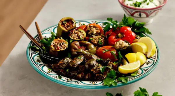 En tallrik med fyllda grönsaker och vinblad, perfekt för ett dolma recept. Serveras med citronklyftor och en skål med yoghurt.