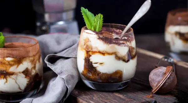 Pyszne tiramisu w pucharkach, udekorowane listkiem mięty i posypane kakao. Idealne na deser.