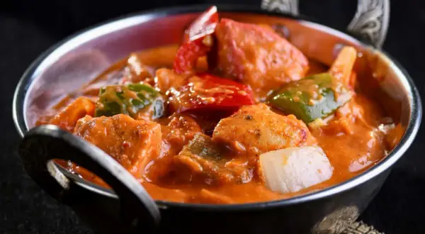 Delicioso pollo al curry con leche de coco, pimientos y cebolla en un cuenco metálico.