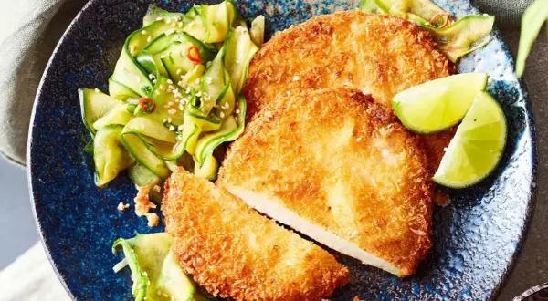Knuspriges Kohlrabi-Schnitzel mit Gurkensalat und Limettenspalten auf einem blauen Teller.