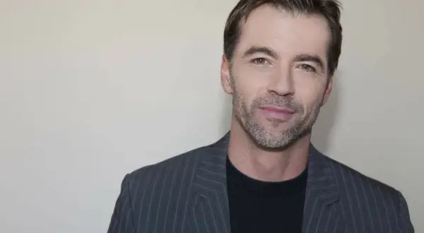 Un homme d'environ 40 ans, le regard franc, porte une veste à fines rayures grises sur un pull noir.