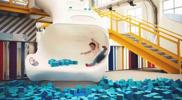 Kind rutscht in Techmania Pilsen durch eine weiße Röhre in einen Pool aus blauen Schaumstoffwürfeln.