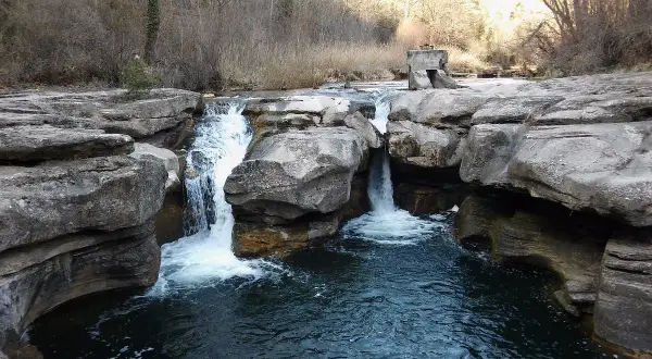 Cascada en la riera del Palau, con rocas erosionadas y vegetación de ribera. El agua cae formando remolinos.