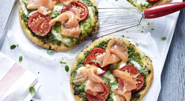 Zwei kleine Pizzen mit Pesto, Tomaten und Lachs auf einem Blech.