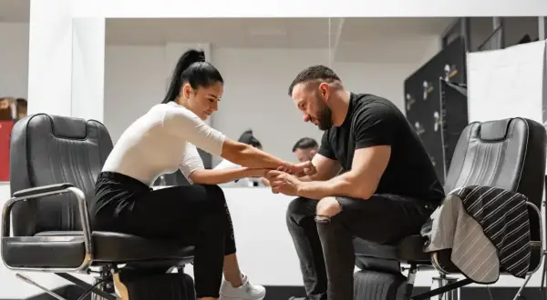 Barber w czarnym t-shircie i podartych jeansach siedzi na fotelu, trzymając dłoń klientki. Zastanawia się, ile zarabia barber.