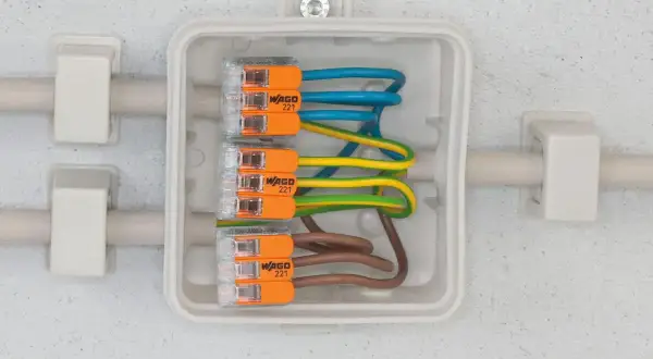 Nowoczesna instalacja elektryczna z kostkami WAGO 221, łączącymi przewody niebieski, żółto-zielony i brązowy w białej puszce.