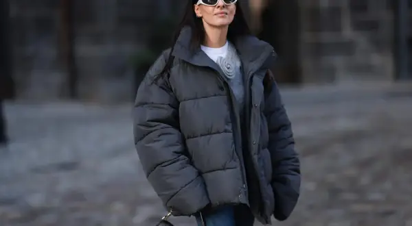 Frau mit Daunenjacke, die sie ohne Trockner wäscht, trägt weiße Sonnenbrille und schwarze Tasche.