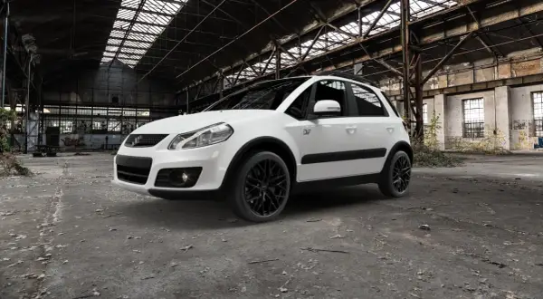Vit Suzuki SX4 med svarta fälgar står i en övergiven lagerlokal. Kanske ett problem med att hitta en ny ägare?