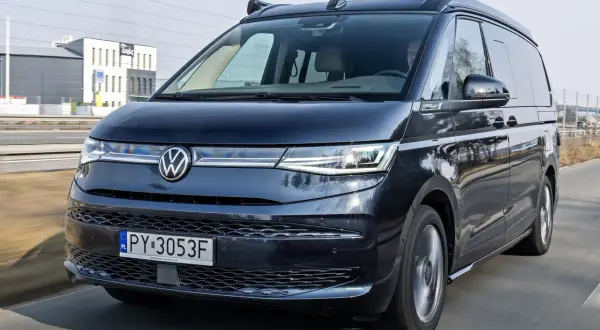 Ciemny Volkswagen California w ruchu drogowym. Sprawdź aktualną volkswagen california cena i planuj podróże!