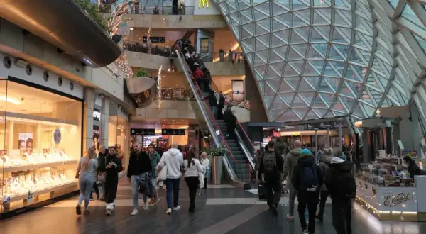 Ludzie w centrum handlowym, schodzą i wchodzą na ruchome schody. Czy 6 stycznia są otwarte sklepy? Widać sklepy z biżuterią i jedzeniem.
