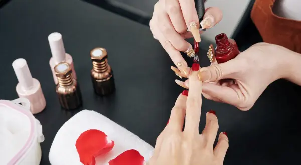 Manicure w trakcie. Stylistka nakłada czerwony lakier. Zastanawiasz się, jak przyspieszyć wysychanie lakieru do paznokci?