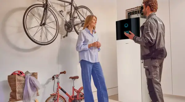 Técnico explica a una mujer el **rendimiento estacional aerotermia** junto a una unidad Daikin. Bicicletas colgadas al fondo.
