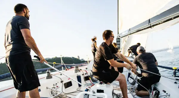 Equipaggio lavora sulle cime de la barca a vela, con un'altra barca in lontananza.