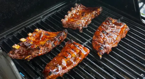 Soczyste żeberka w marynacie do żeberek skwierczą na grillu, nabierając apetycznego koloru.