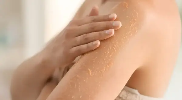 Mano che applica scrub corpo per esfoliare e rendere la pelle liscia e luminosa. Scopri a cosa serve lo scrub corpo.