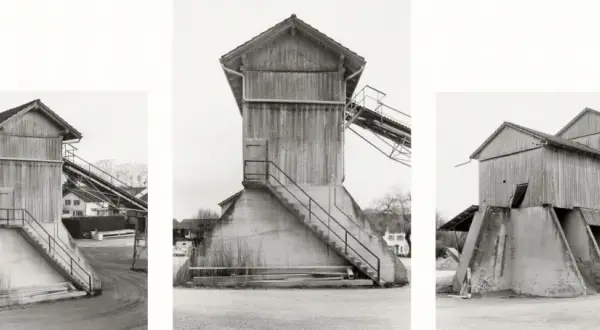 Strutture industriali in legno e cemento, tipiche delle opere di Hilla Becher, con scale esterne e nastri trasportatori.