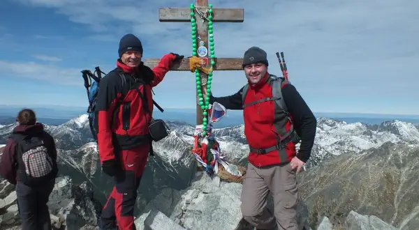 Dwóch turystów na szczycie w Tatrach Wysokich 2494 m, przy drewnianym krzyżu ozdobionym zielonymi paciorkami.