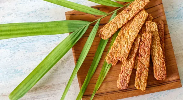 Knusprige Tempeh-Sticks auf einem Holzbrett, garniert mit grünen Blättern. Ein leckeres Tempeh-Rezept für gesunde Ernährung.