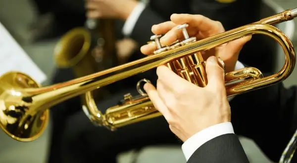 Hände spielen eine glänzende Trompete. Ein Musiker bereitet sich auf sein Referat vor, während im Hintergrund ein Saxophon zu sehen ist.