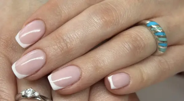 Dłonie z klasycznym french manicure, zdobione subtelnym wzorkiem. Na palcach błyszczą pierścionki.