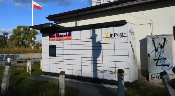 Paczkomat InPost z logo Allegro Smart. W tle polska flaga i budynek. Ile jest paczkomatów w Polsce? Tysiące!