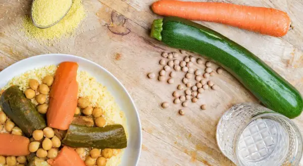 Un plat de couscous aux légumes, pois chiches, carottes et courgettes. Une cuillère de semoule est à côté.
