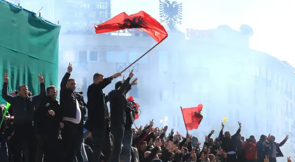 Människor viftar med albanska flaggor och gör fredstecken. En del av folkmassan verkar fira, vilket ger en känsla av stolthet och gemenskap. Detta kan vara en del av fakta om Albanien.