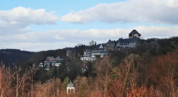 Blick auf Schloss Burg, das majestätisch auf einem Hügel thront, umgeben von Bäumen. Ein kleiner Pavillon im Vordergrund, im winterlichen Wupper Tal.