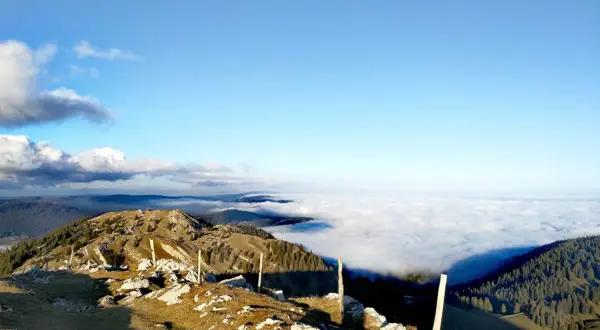 Vue panoramique d'une randonnée la Dôle depuis les Dappes, avec une mer de nuages sous un ciel bleu éclatant.
