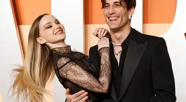 La pareja Dove Cameron y Dylan Sprouse ríen juntos, ella con un vestido de encaje negro y él con un traje negro.