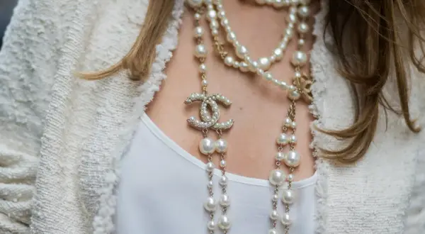 Eleganckie stylizacje z perłami: wielowarstwowy naszyjnik z logo Chanel i perłami na tle białej marynarki.