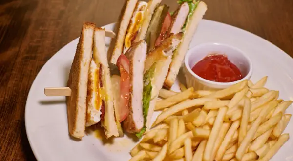 Idealne przekąski do piwa: chrupiące frytki i soczyste kanapki club sandwich z kurczakiem, bekonem i jajkiem.