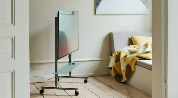 Moderner fernseher im schlafzimmer auf einem grünen Rollwagen, daneben eine gemütliche Bank mit karierter Decke.
