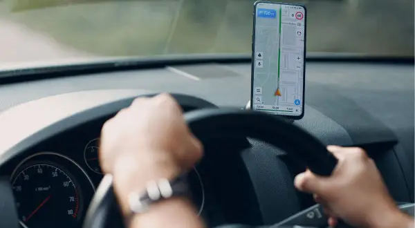Ręce na kierownicy, smartfon z nawigacją na Androida pokazuje trasę.