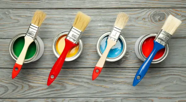 Quattro barattoli di vernice colorata (verde, giallo, blu, rosso) con pennelli pronti all'uso. La scelta della vernice giusta per il legno è fondamentale per un buon risultato.