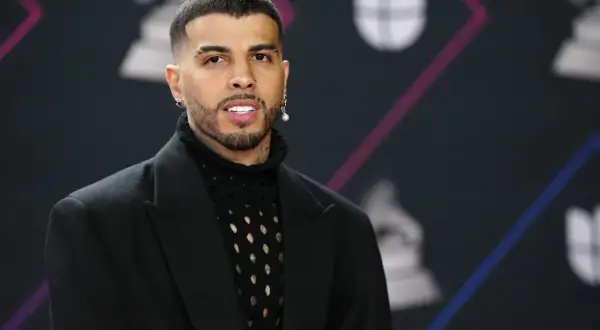 Rauw Alejandro, de Puerto Rico, posa con un traje negro y un suéter de red.