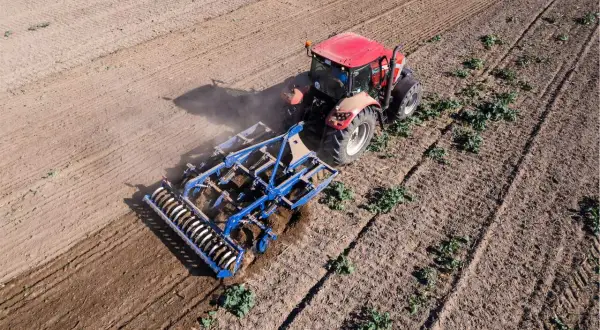 Un tracteur rouge travaille le sol avec un cultivateur, préparant le terrain pour la culture sans labour.